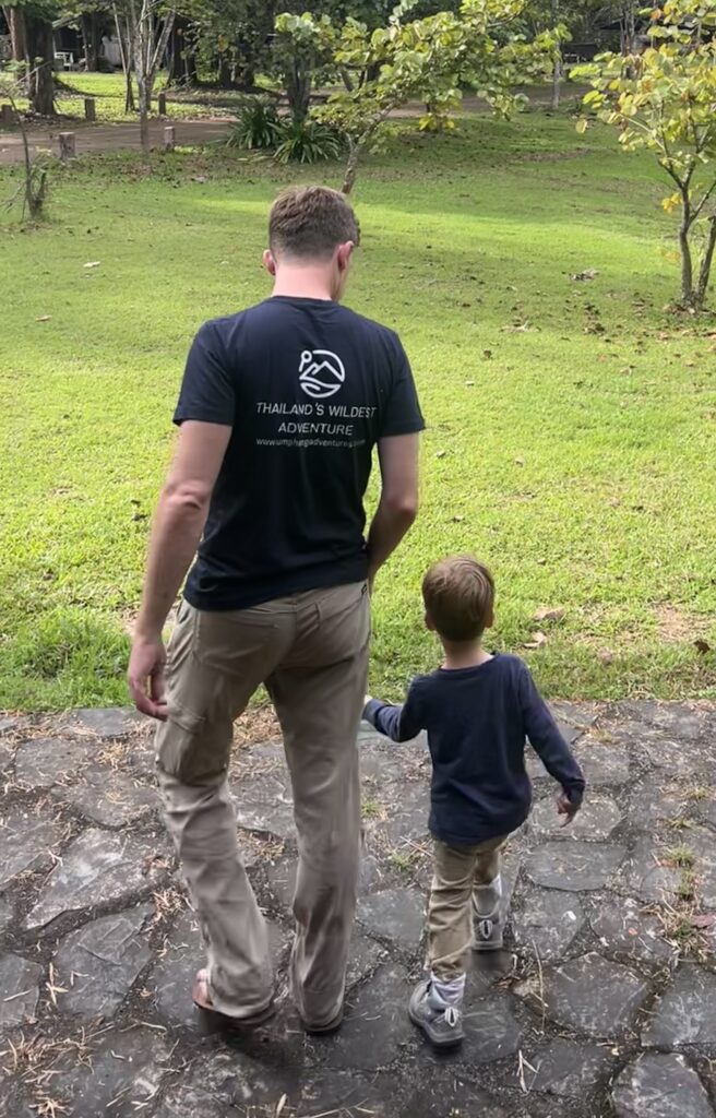 Father and young son holding hands and walking away on a stone path, representing a family adventure and the start of a long trek in Umphang.