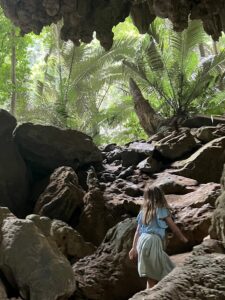 A small girl backlit as she emerges from a cave into a palm forest