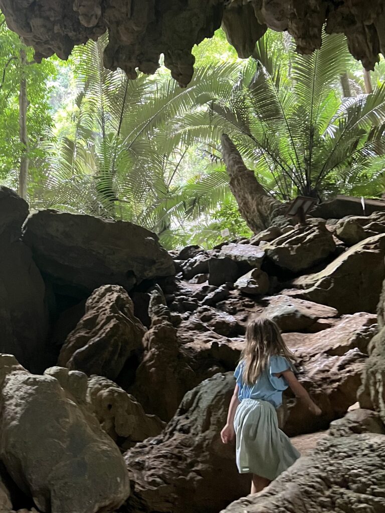 A small girl backlit as she emerges from a cave into a palm forest