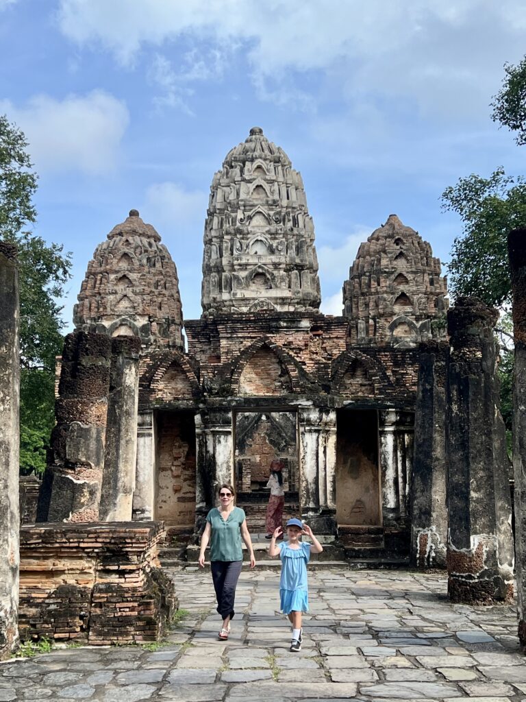 A mother and child walking towards the three distinctive Khmer-style prangs of Wat Si Sawai in the Central Zone of Sukhothai Historical Park.