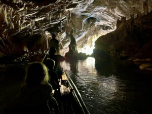 A family on a bamboo raft guided by a kerosene lantern through the dark, limestone Tham Nam Lod cave in Mae Hong Son, Thailand.