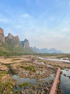 Bueng Bua Boardwalk stretching across the Thung Sam Roi Yot Freshwater Marsh, with jagged limestone mountains (karsts) of Khao Sam Roi Yot National Park in the background.