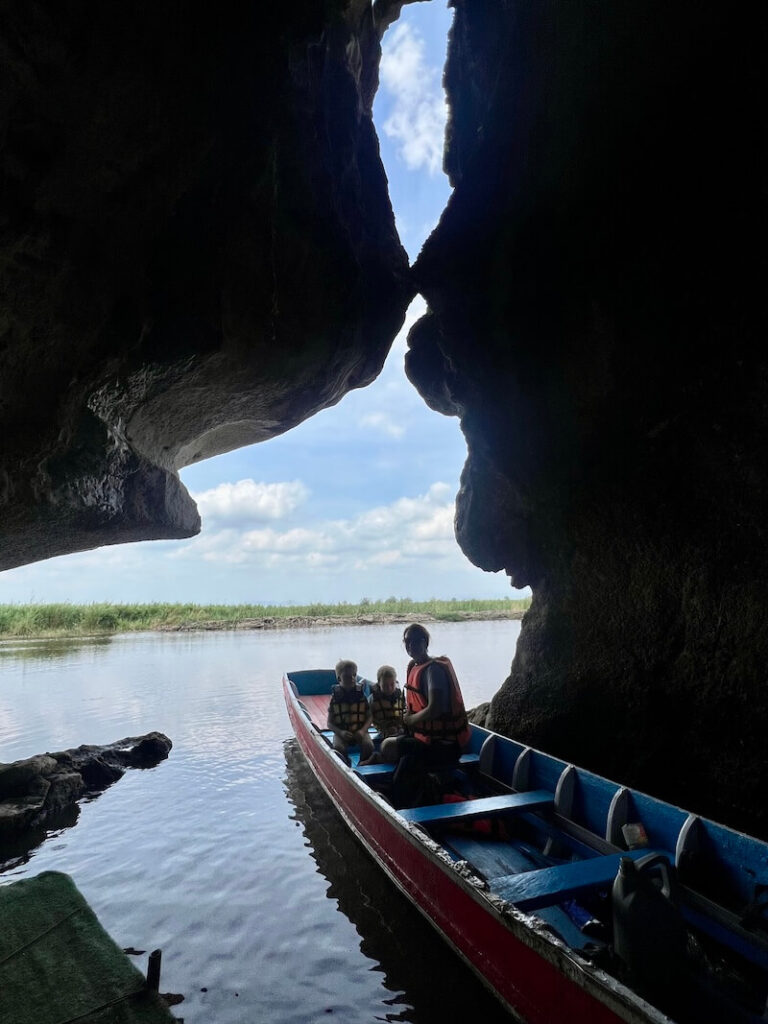A family sitting in a longtail boat silhouetted by the opening of the Kissing Cave (Khao Joop Gan), showing the unique rock formation where the two limestone faces almost touch.