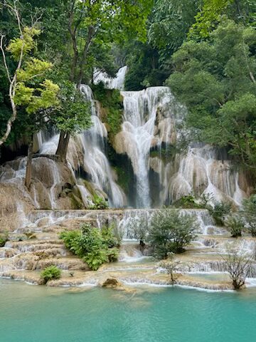 The multi-tiered, cascading turquoise pools of Kuang Si Falls in Luang Prabang, Laos, surrounded by lush green jungle and rock terraces.