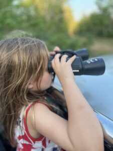 A child peering through large binoculars from the safari truck, looking out over the landscape during a wild elephant safari at Kui Buri National Park, Thailand.