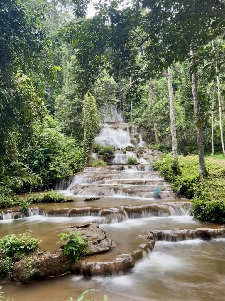 Long exposure photo of Pha Charoen Waterfall's 97 limestone terraces cascading through lush jungle in Umphang, Thailand.