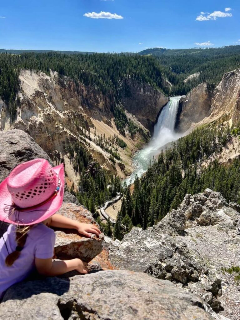 Young girl in a pink cowboy hat looking down at the massive Lower Falls and Grand Canyon of the Yellowstone River.