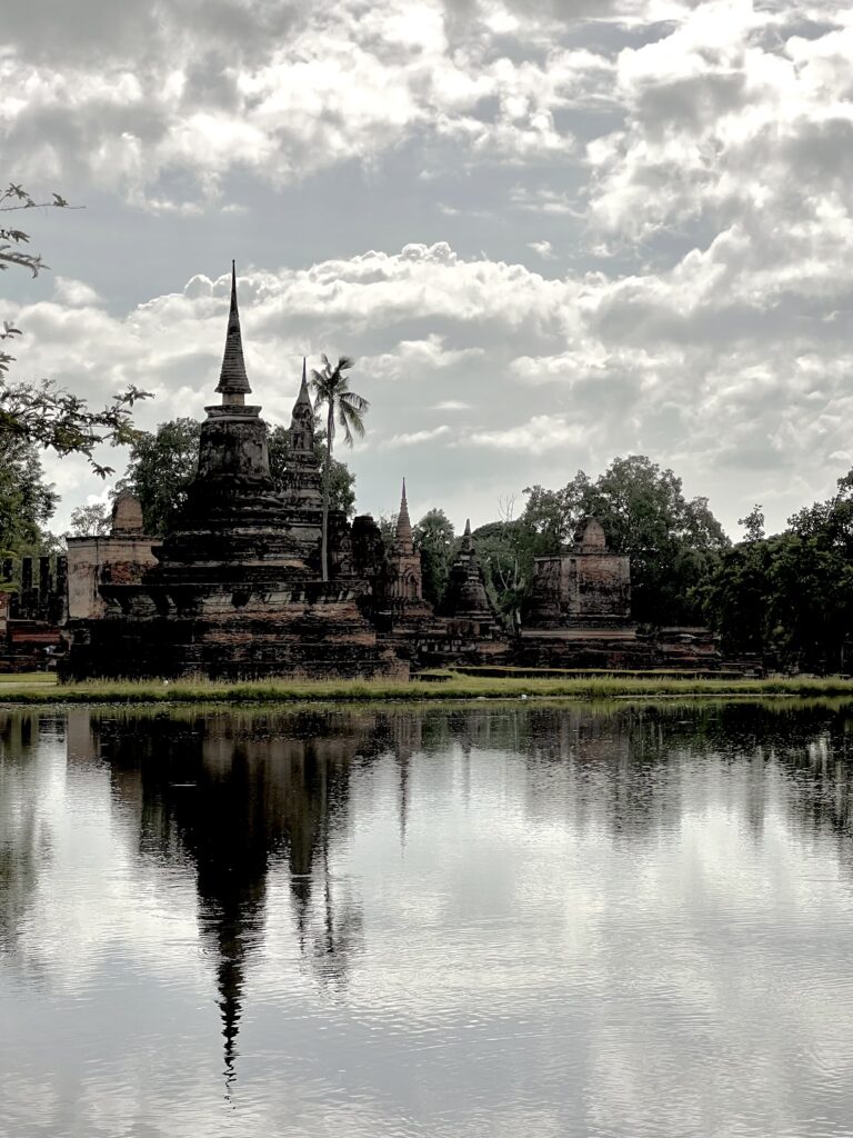 Ancient temple spires and ruins of Wat Mahathat reflecting clearly in the still water of the surrounding reservoir in Sukhothai Historical Park.