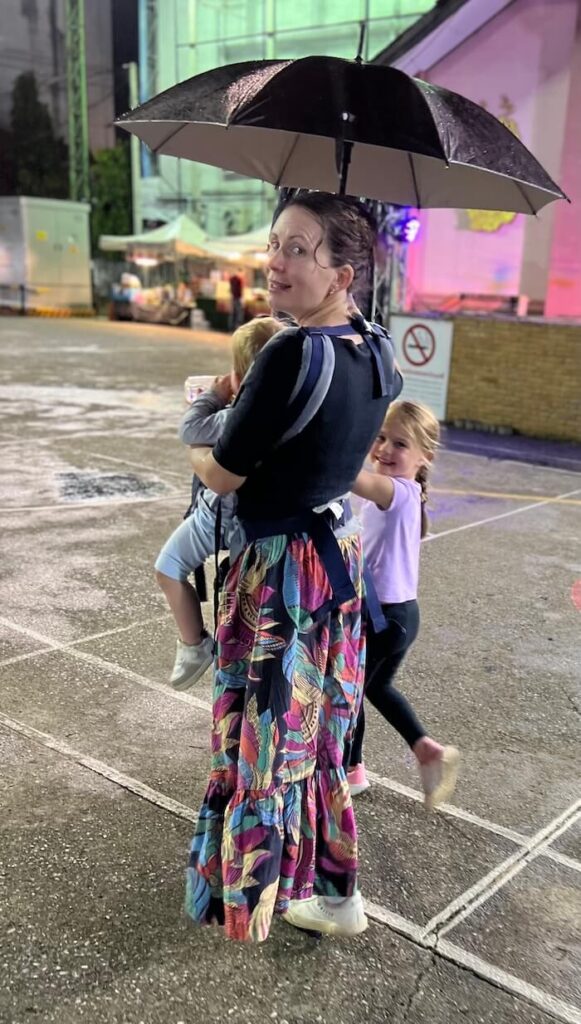 Mother holding child under umbrella walking home from Chiang Rai night market in the rain