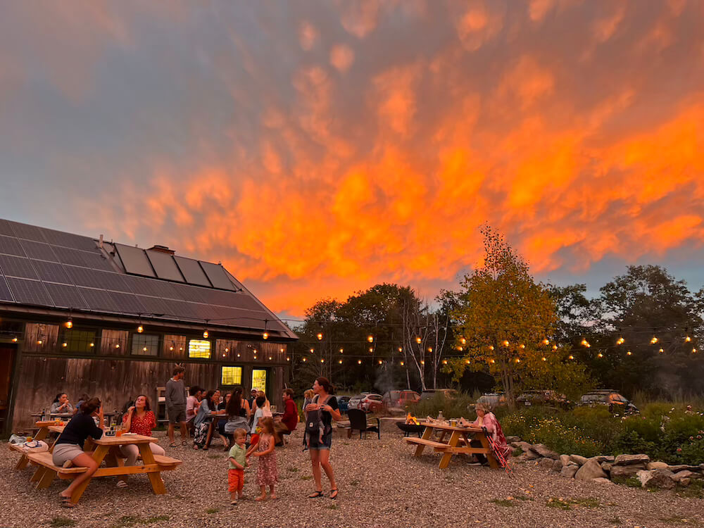 Family and travelers gathered outdoors at sunset for dinner under string lights