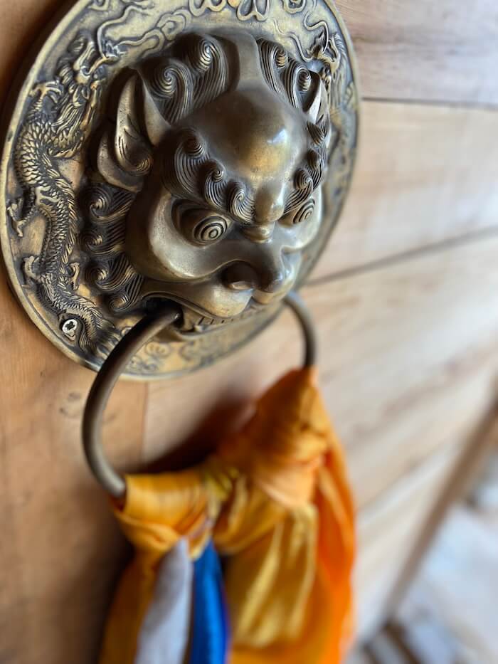Close-up of a detailed brass lion door knocker with colorful offering ribbons