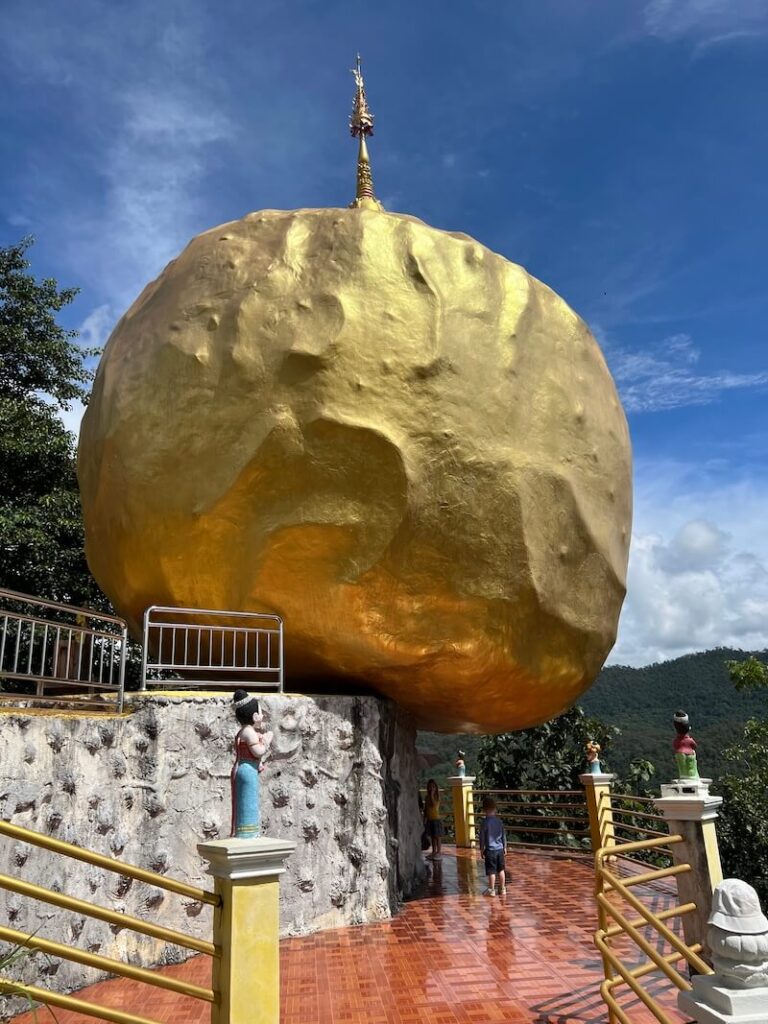 A large precariously balanced golden boulder with a hti crown atop a limestone cliff at Wat Phra That Doi Mon Ching in Chiang Dao.