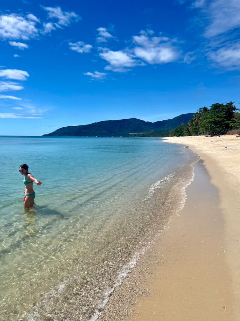 Woman wading in clear, calm turquoise water on a secluded beach with mountains in the background at Khanom, Thailand.