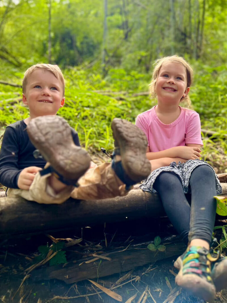 Two young children smiling during a break on a lush green jungle trail in Chiang Dao, Northern Thailand.