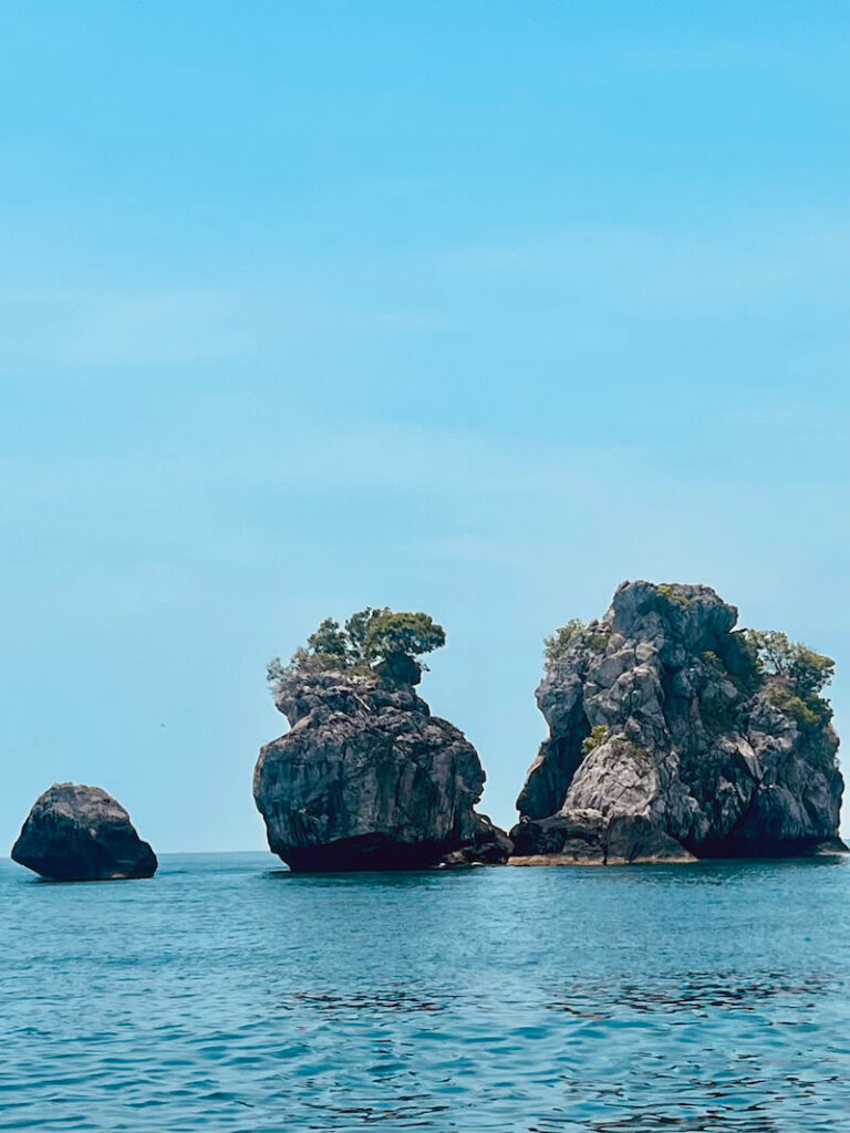 Three massive, jagged rock formations (islets) rising vertically from the blue ocean in the Mu Ko Chumphon National Park, Thailand.
