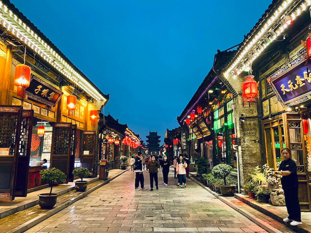 Illuminated traditional Chinese street at night with red lanterns and travelers walking