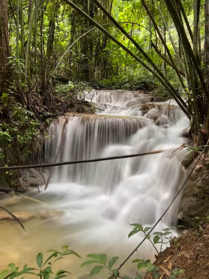 Wide view of the tiered Phu Kaeng Waterfall, framed by dark jungle foliage and bamboo stalks in Doi Luang National Park, Chiang Rai.
