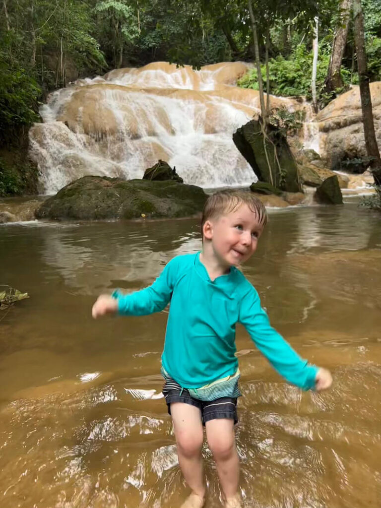 A young boy in a turquoise swim shirt dancing in the water at the base of the Sri Sangwan sticky waterfall in Chiang Dao.