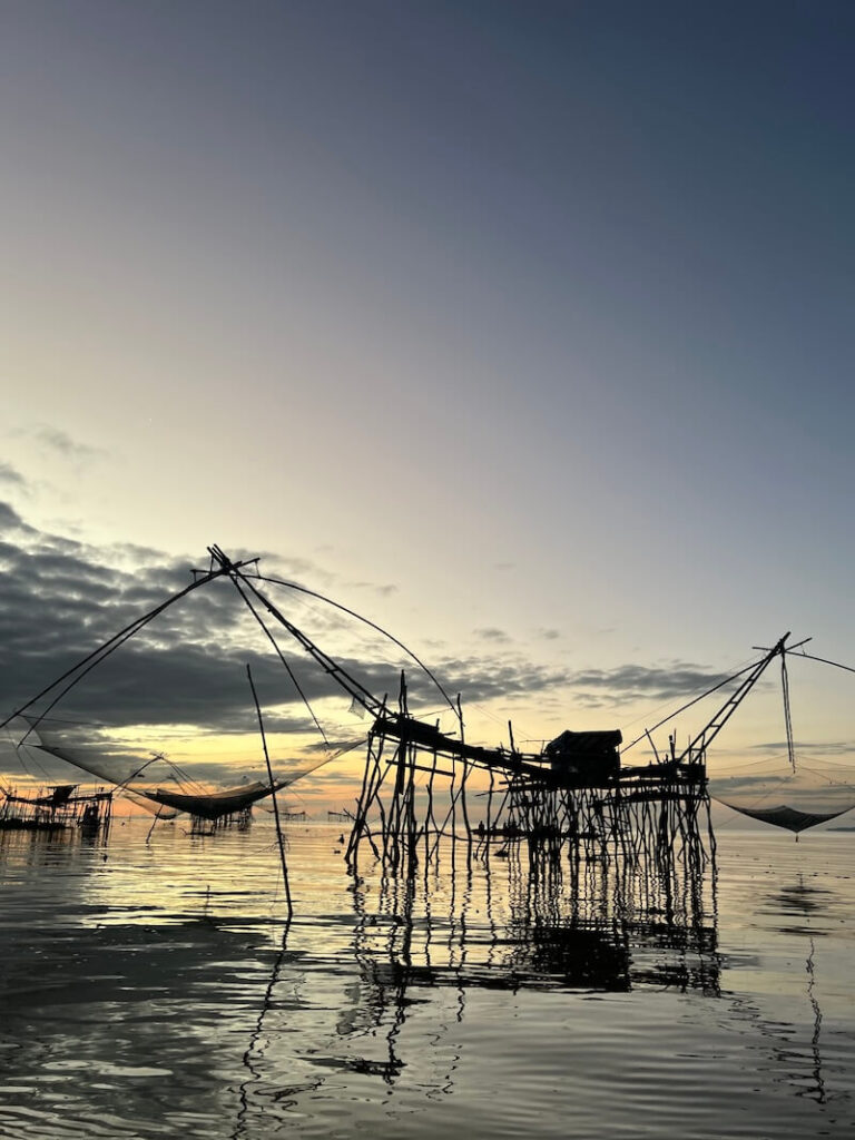 Sunrise silhouette of the traditional stilted Yor Yak (giant lifting nets) fishing traps reflected in the calm water of the Thale Noi wetlands, Phatthalung.