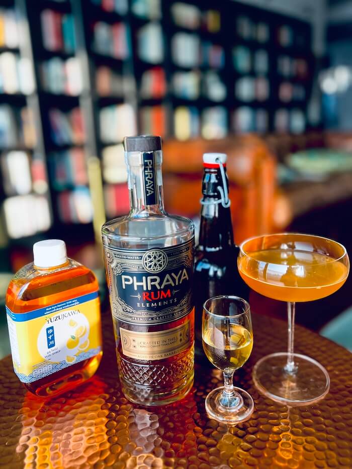 The Bee’s Shortcut cocktail in a couple glass with a bottle and glass of mead, a bottle of yuzu syrup, and a bottle of Phraya Elements.