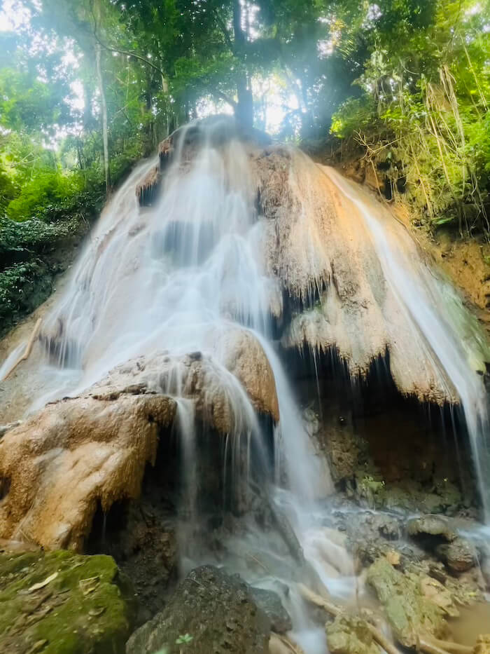 The Splendid Namtok Nam Min A long-exposure shot of Nam Min Waterfall in Phayao, showing water cascading over orange limestone curtains surrounded by lush jungle greenery.