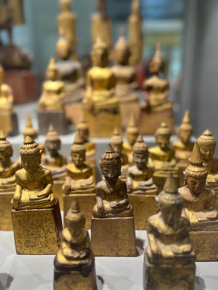 A collection of small, weathered wooden Buddha statues covered in gold leaf at the Nan Provincial Museum.
