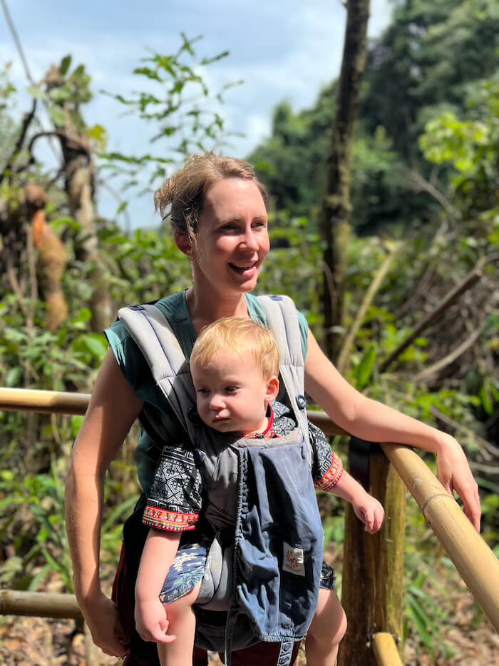 A mother carrying her young child on her back/in her arms while walking through the lush forest trails of Doi Inthanon National Park.