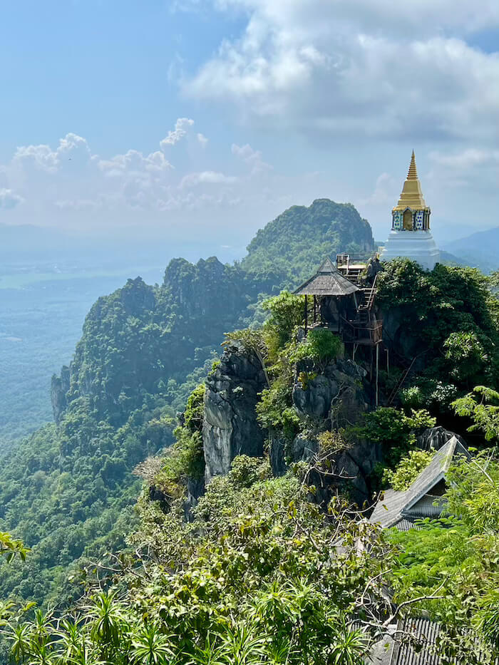 A golden-topped white pagoda perched on a dramatic limestone peak at Wat Chaloem Phra Kiat, overlooking a lush green valley in Lampang.