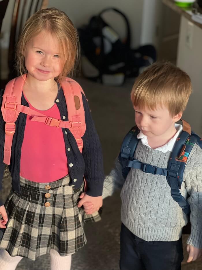 Two young children wearing adventure backpacks and holding hands, ready for a worldschooling lesson.