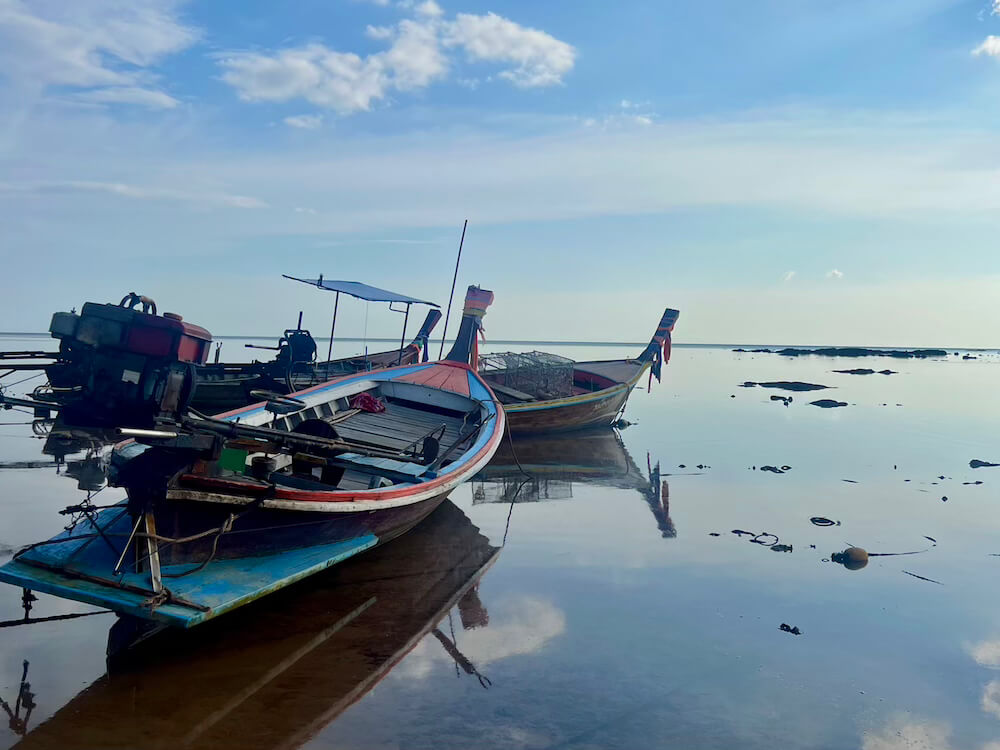 Longtail boats sitting at low tide on Koh Libong, Thailand.  The boats are reflected in the smooth, still water which acts like a mirror of the sky above.
