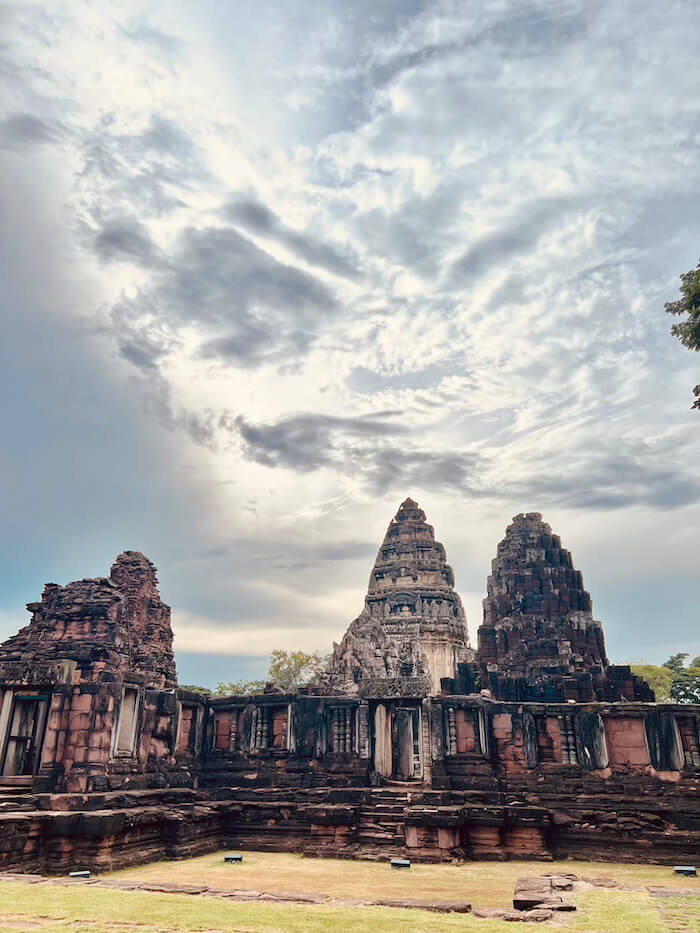 The dark stone towers and weathered walls of Phimai Historical Park standing under a dramatic, cloudy sky.