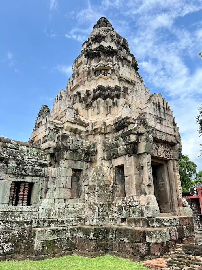 The central stone prang of Phimai Historical Park under a blue sky, showing intricate Khmer carvings and tiered architecture.