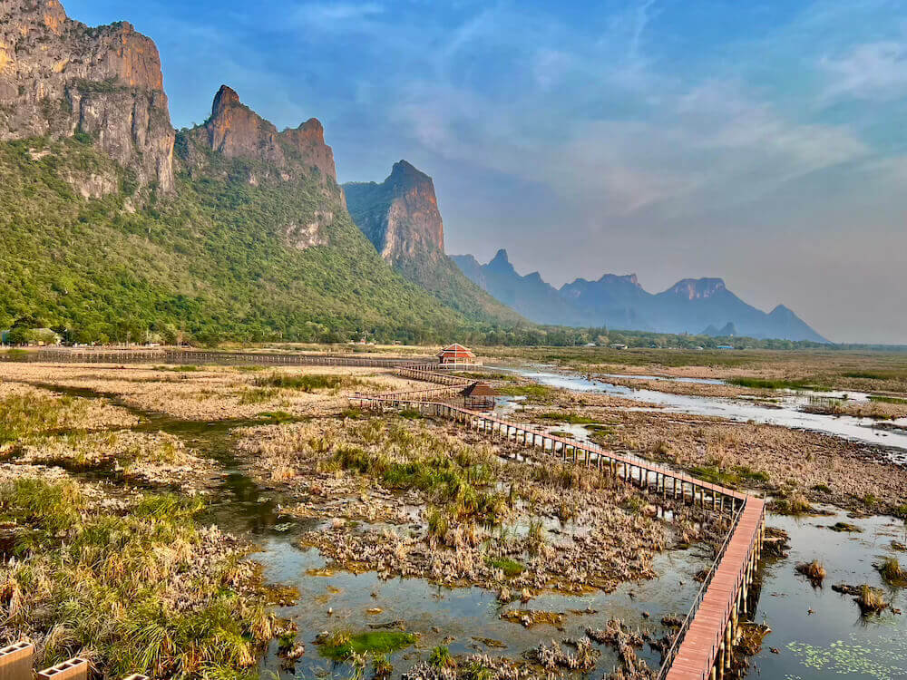 A long wooden boardwalk winding through the Thale Noi wetlands with dramatic limestone karst mountains in the background at Sam Roi Yot National Park.