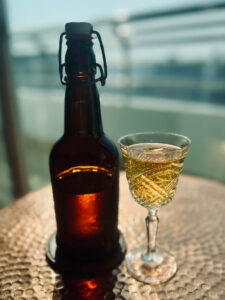 A swing-top bottle and a crystal glass filled with golden Thai wild honey mead on a balcony overlooking the Bangkok skyline.