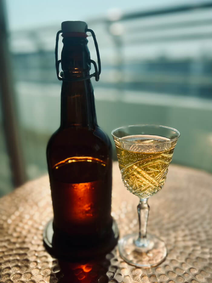 A swing-top bottle and a crystal glass filled with golden Thai wild honey mead on a balcony overlooking the Bangkok skyline.