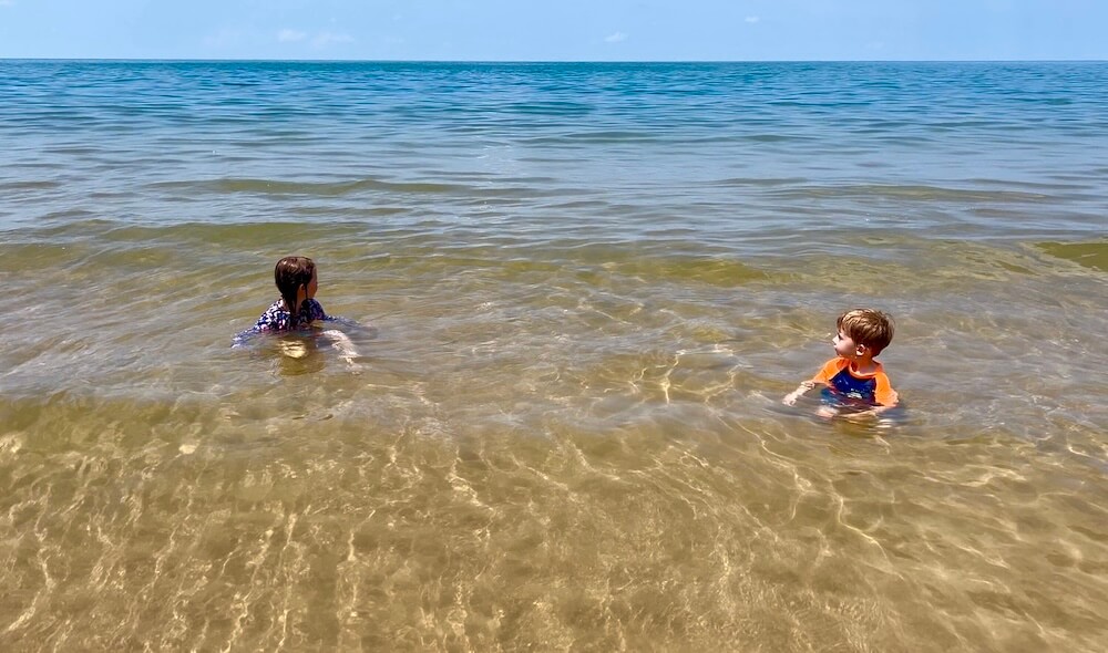 Two young children sitting in the clear, shallow, turquoise water of Ao Krathing beach on a sunny day.