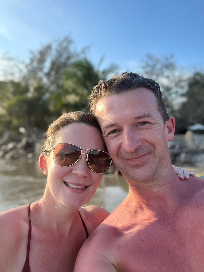 Beachside in Rayong A man and woman smiling for a selfie on a beach in Rayong, Thailand, with the late afternoon sun casting a warm glow over the coastal background.