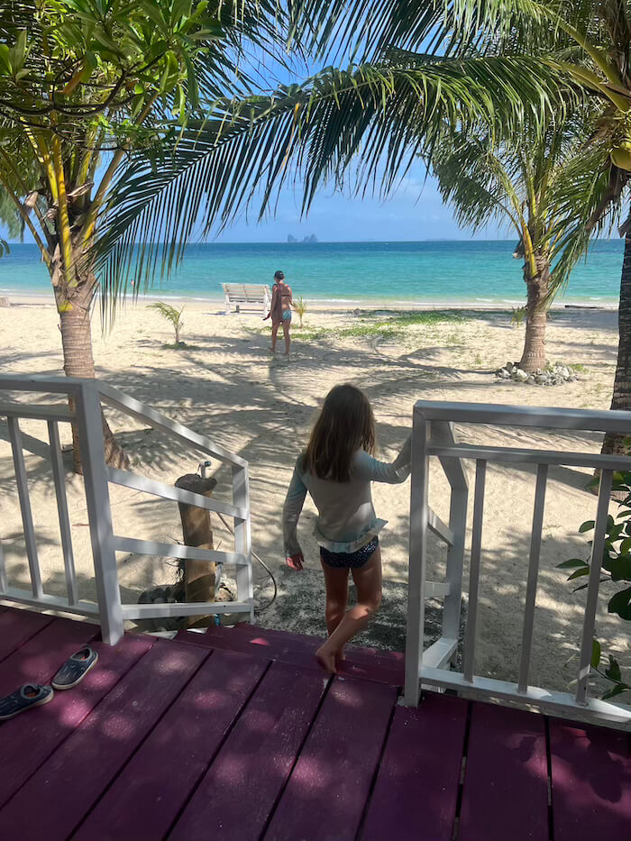 Front-Row Seats to Paradise A view from the wooden steps of a beach bungalow looking out through palm trees toward a turquoise sea on Koh Bulon Lae.