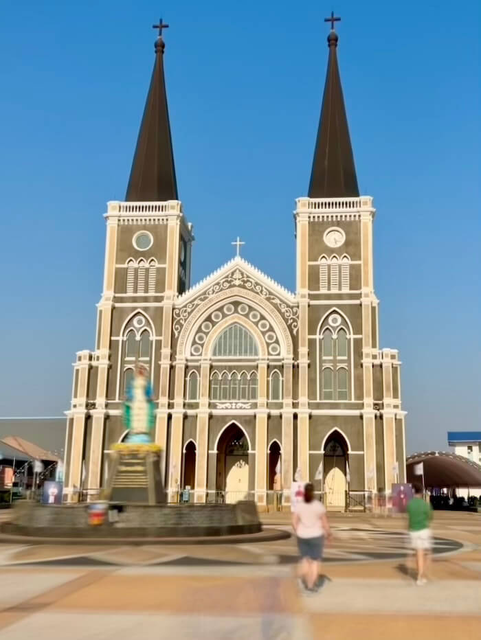 The twin spires of the Gothic Revival Cathedral of the Immaculate Conception in Chanthaburi, Thailand, under a clear blue sky.