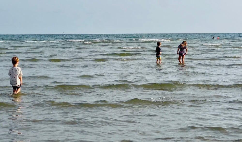 Three young children wading in the shallow, glittering water of Chao Lao Beach in Chanthaburi at low tide.