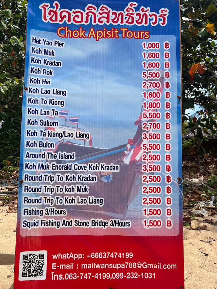 Koh Libong Boat Tour Prices A red and blue price board for Chok Apisit Tours on Koh Libong, showing boat transfer and tour costs to places like Koh Kradan, Koh Lao Liang, and Koh Muk.