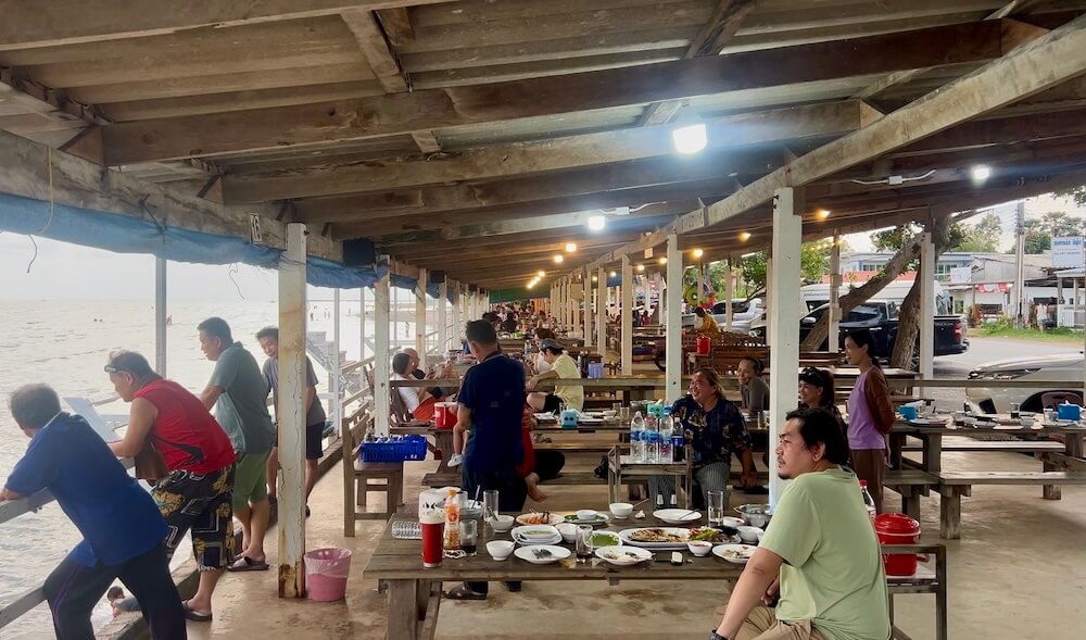Outdoor beachfront dining area at Kho Khao Seafood in Chanthaburi, featuring wooden tables under a sheltered pavilion along the sea wall.