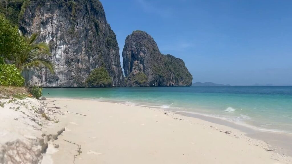 Paradise Found on Koh Lao Liang A pristine, empty white sand beach on Koh Lao Liang South, bordered by turquoise water and soaring limestone karst cliffs under a clear blue sky.