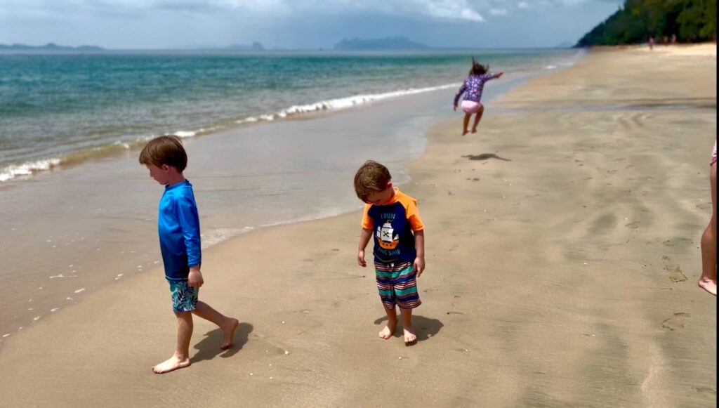 The Secluded Sands of Tung Yaka Three children playing on the caramel-colored sands of Tung Yaka Beach on Koh Libong, with one child jumping for joy in the background and a turquoise sea to the left.