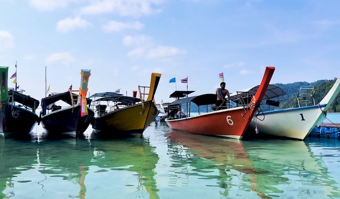 A row of brightly colored longtail boats in shades of red, yellow, and blue floating in the calm, clear turquoise water of the Surin Islands.