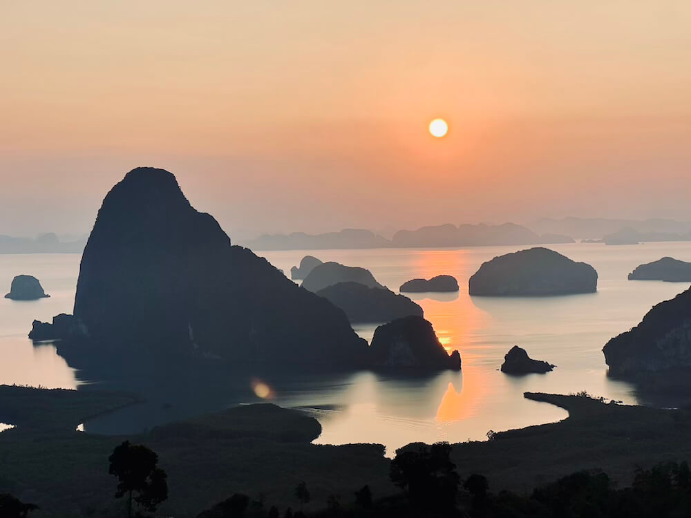 A wide panoramic landscape shot of the golden sunrise over the karst islands and misty waters of Phang Nga Bay from Samet Nangshe Viewpoint.