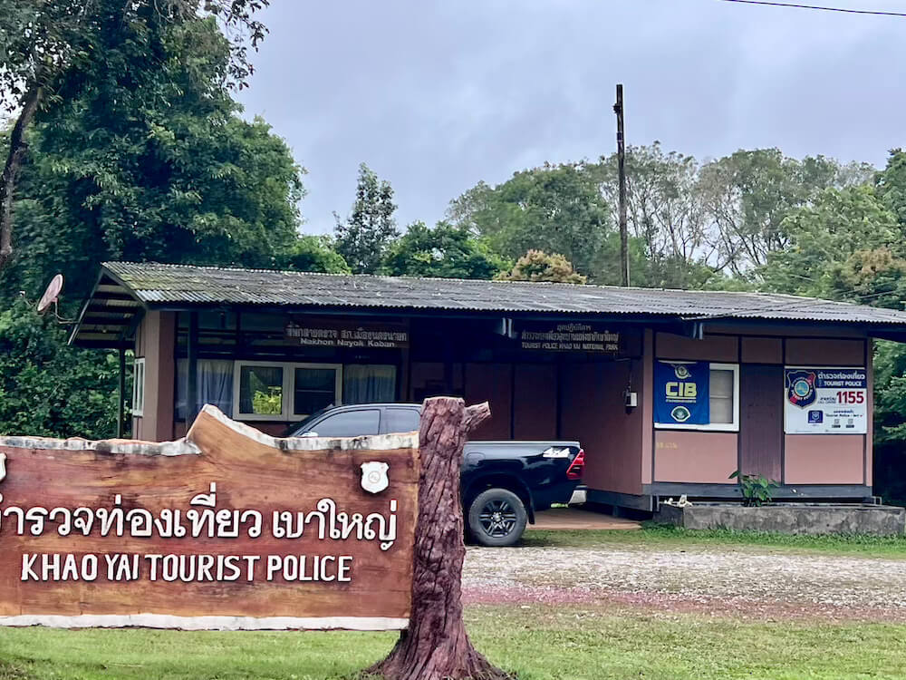 A carved wooden sign reading Khao Yai Tourist Police in front of a small police station building with dense trees behind it.