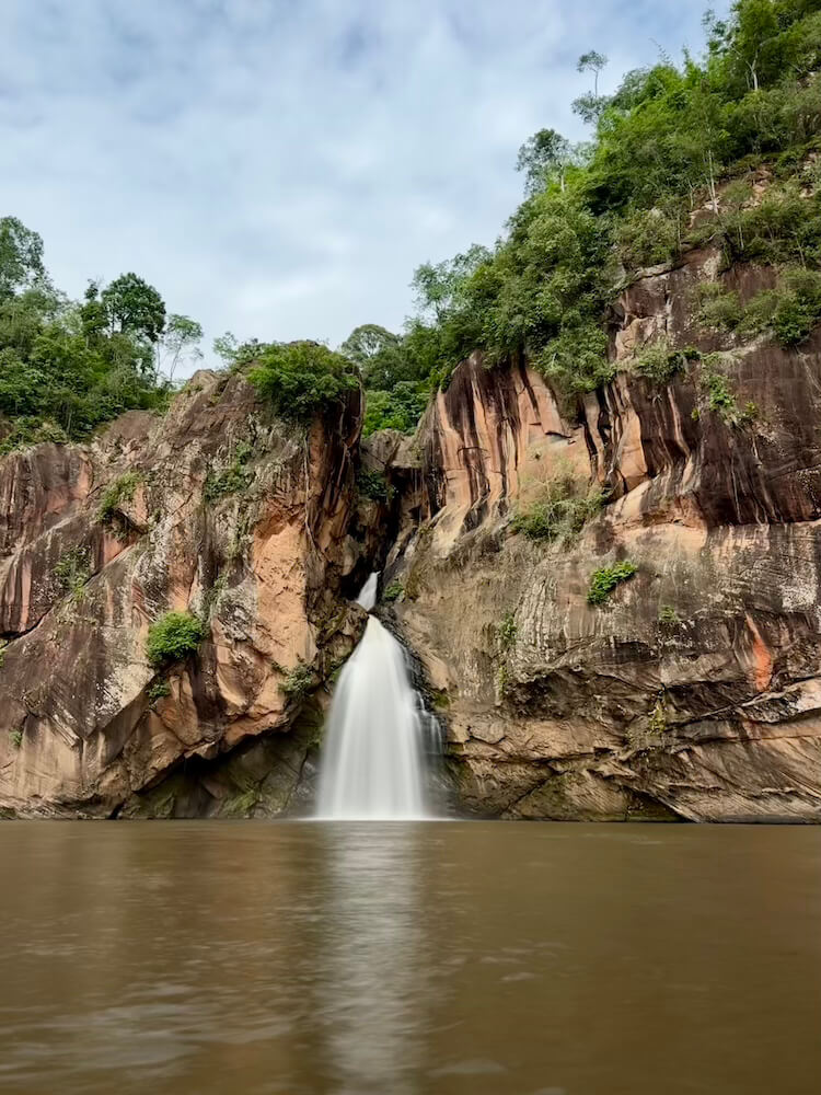 A powerful waterfall pouring through a cleft in massive sandstone cliffs into a wide natural pool
