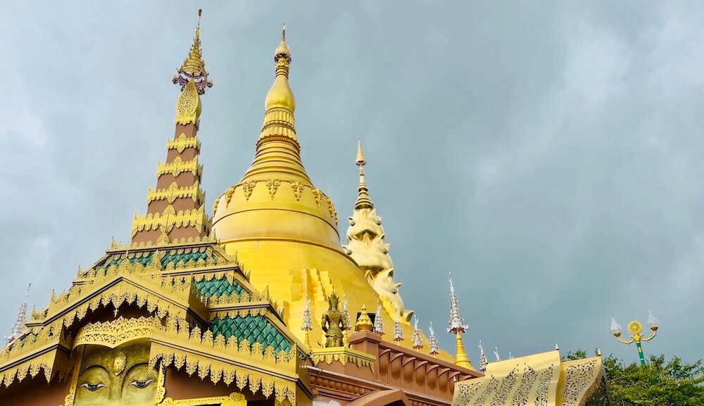 Ornate golden chedis and intricate tiered spires against an overcast sky at Wat Phra That Pha Sorn Kaew.
