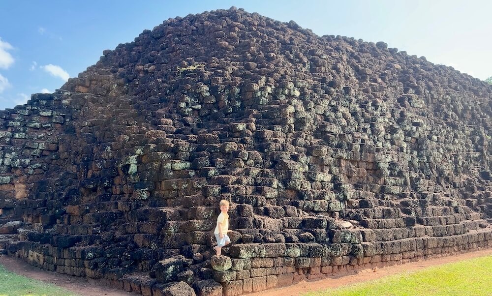 A young boy standing on the lower steps of the ancient laterite stone mound at Khao Khlang Nai in Si Thep Historical Park.